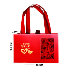 Red gift bag with 'LOVE' and heart designs, containing red roses, on a white background.